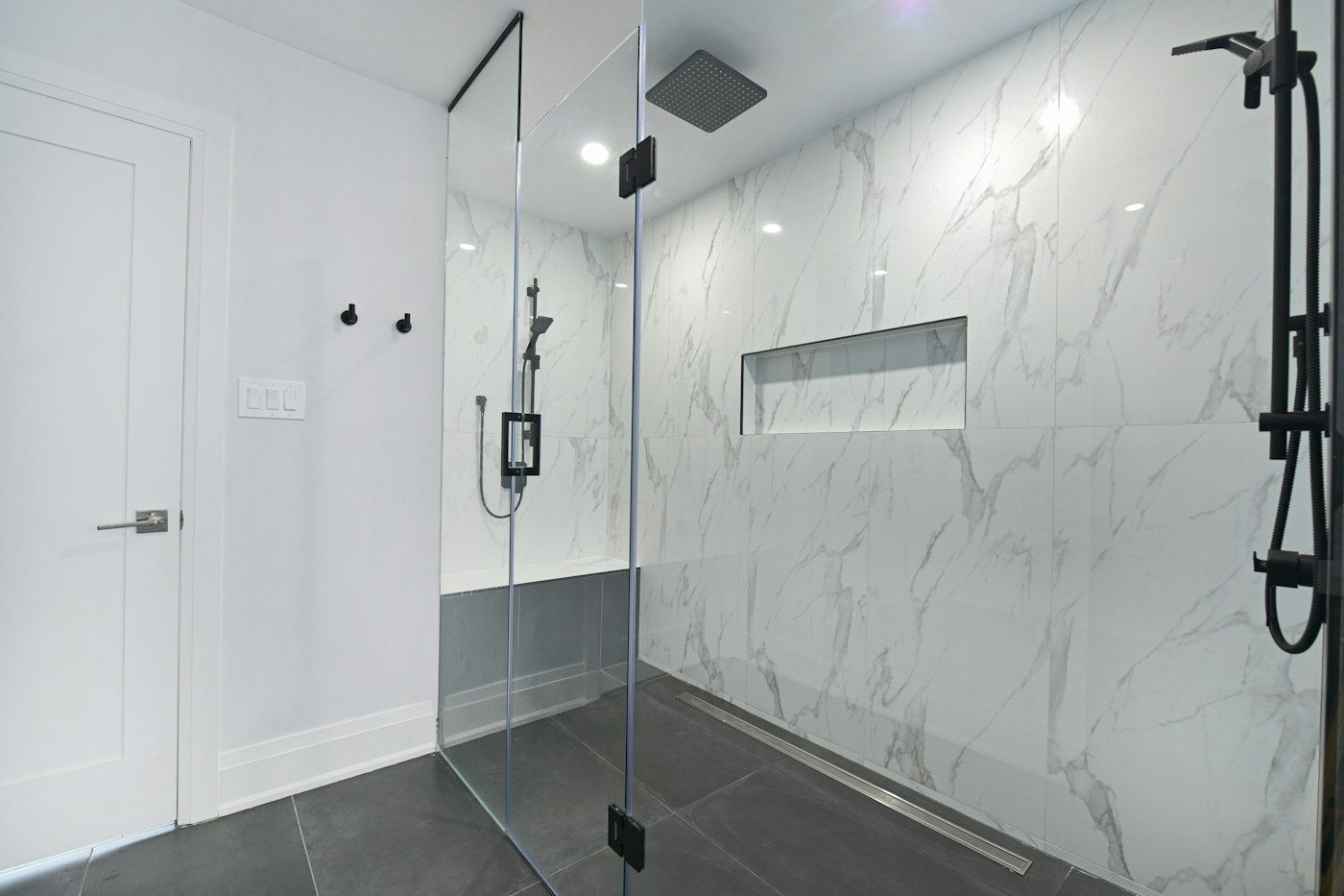 Box de vidro sem moldura com porta de abrir e dobradiças pretas em banheiro de mármore branco