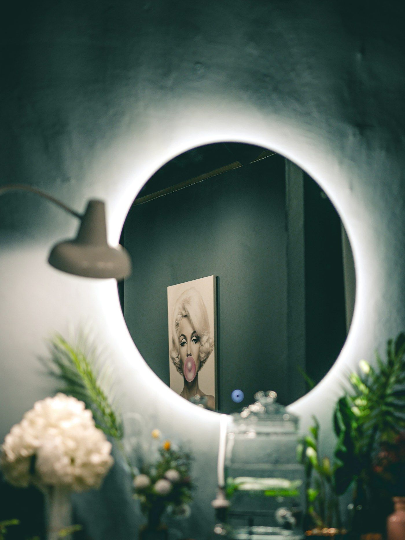 Espelho redondo retroiluminado em parede verde-escura com flores