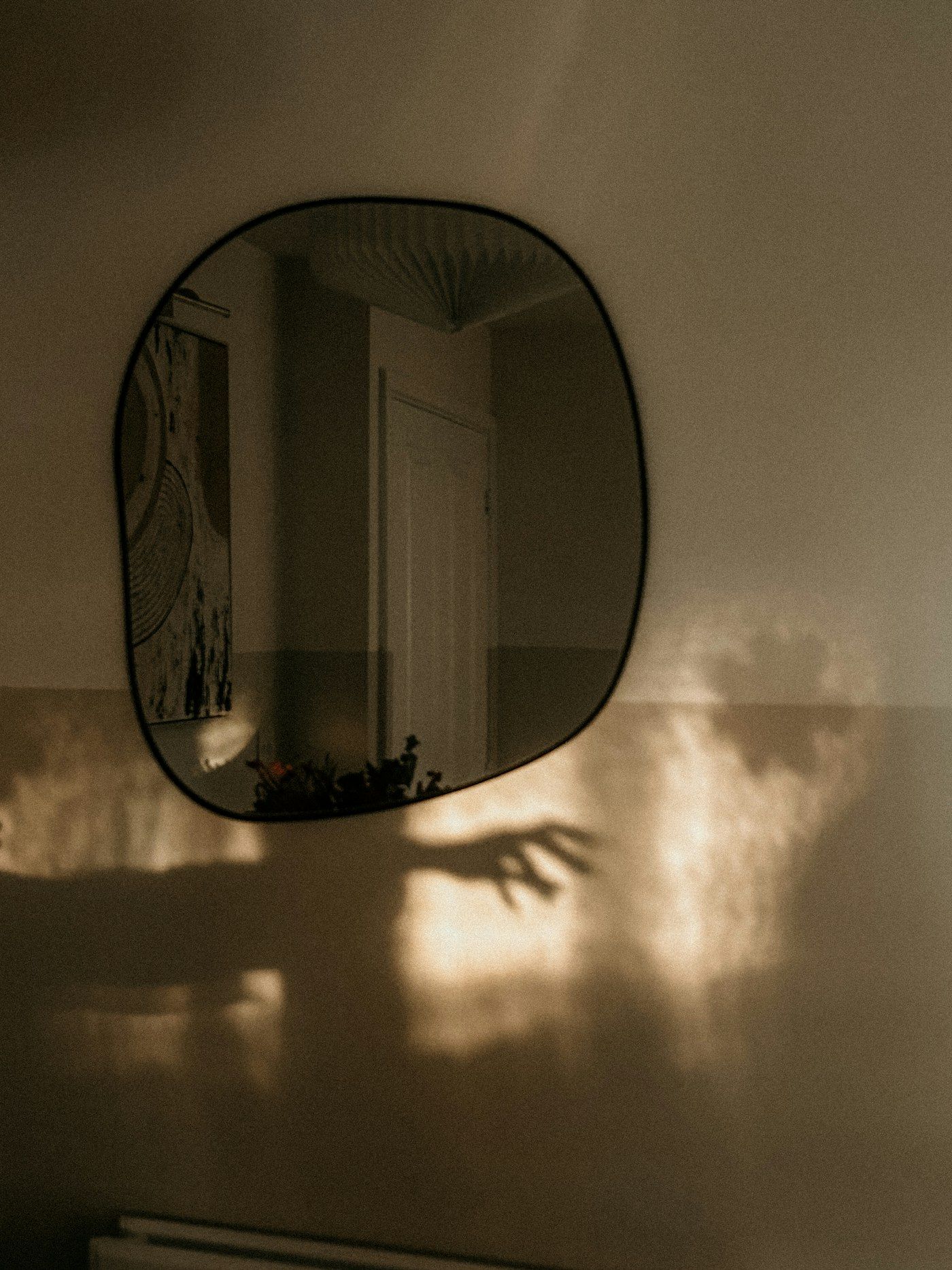 Espelho de contorno orgânico em parede clara com luz natural lateral