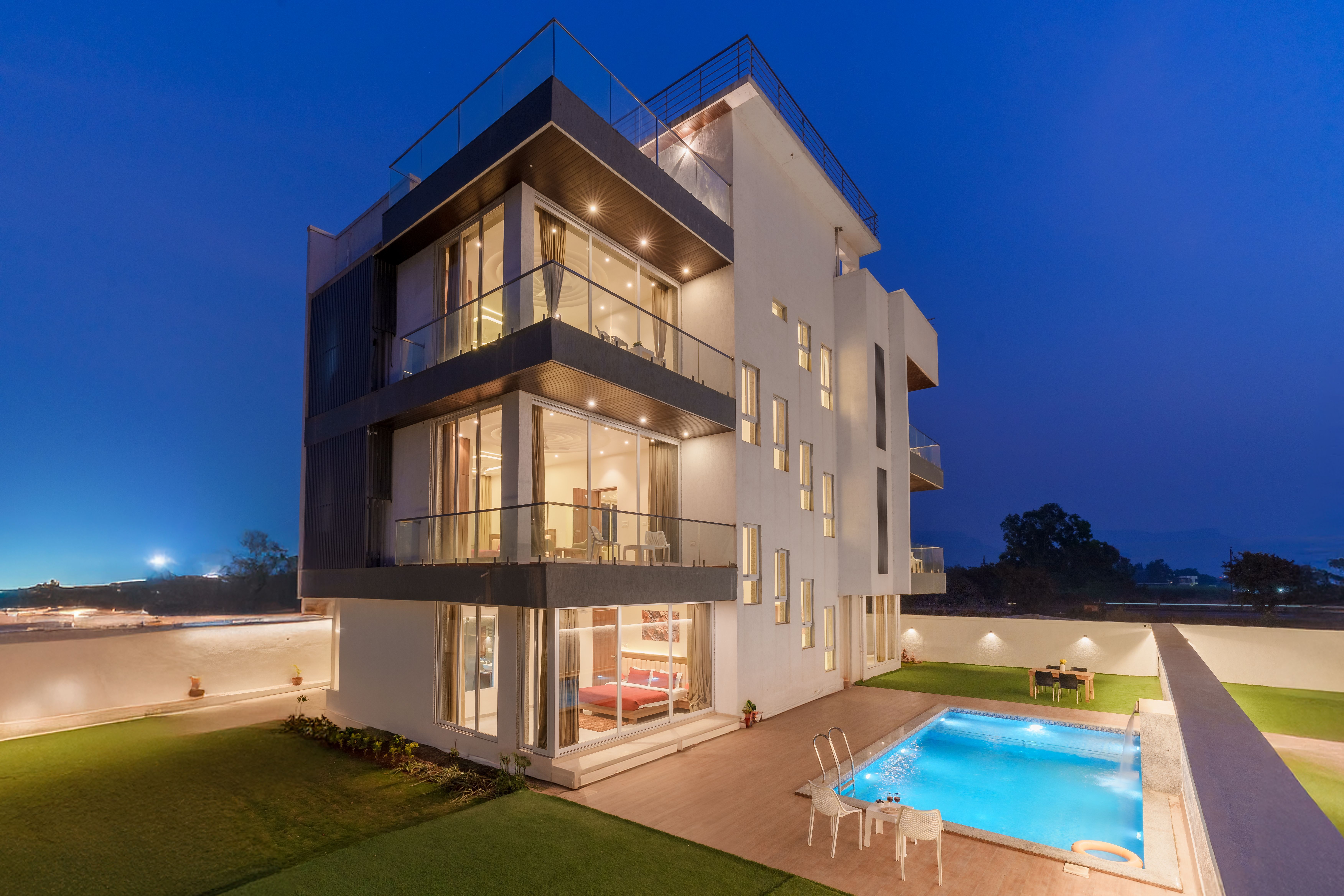 Fachada residencial contemporânea à noite, com varandas de vidro iluminadas e piscina